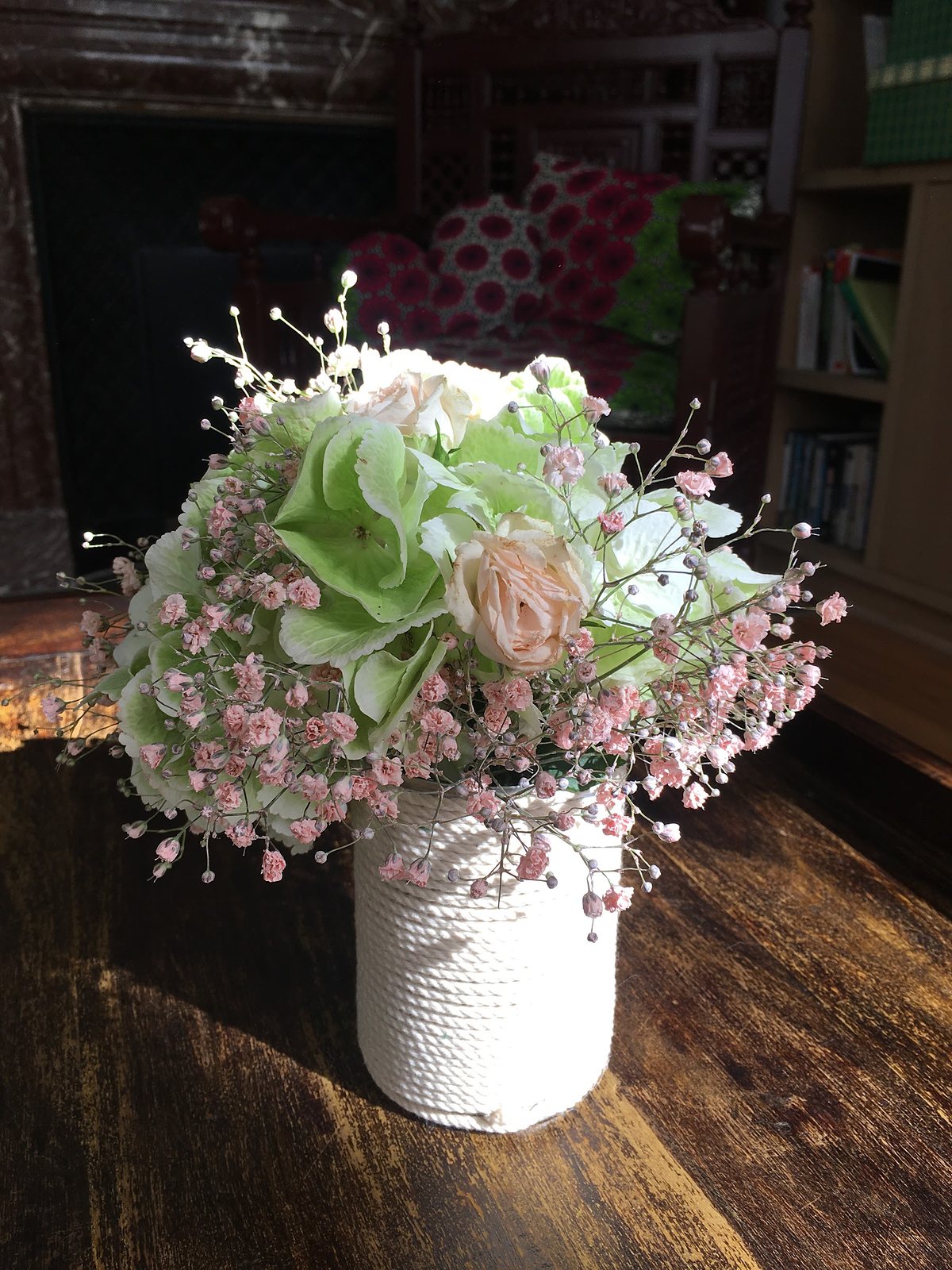 Composition blanche et verte dans un vase blanc, sur une table de bois