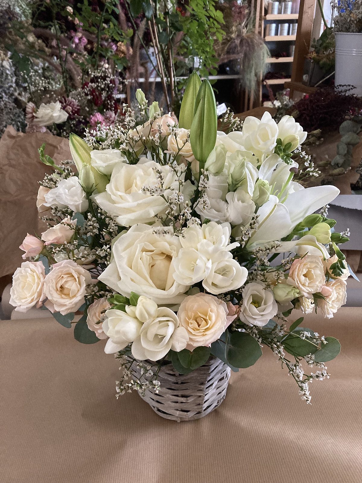 Composition blanche en panier d’osier : lys, roses et gypsophile