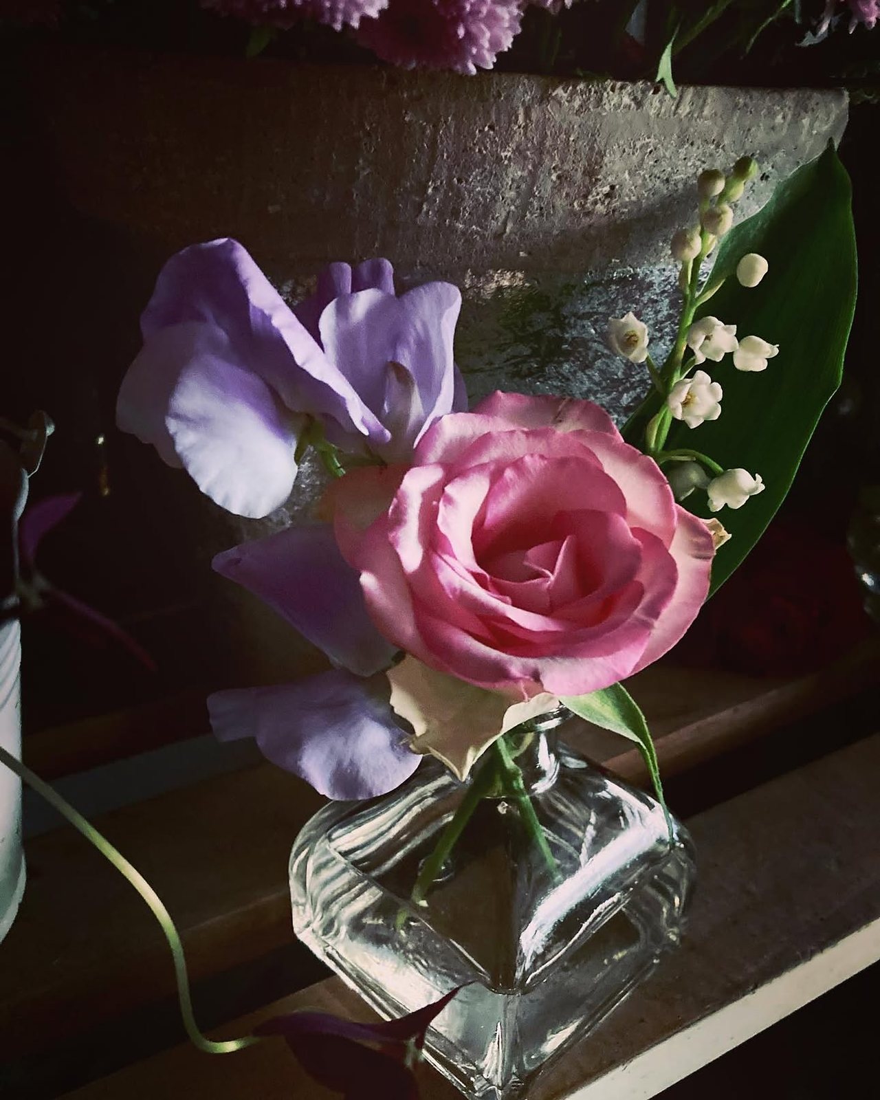 Une rose et un brin de muguet dans un petit vase de verre